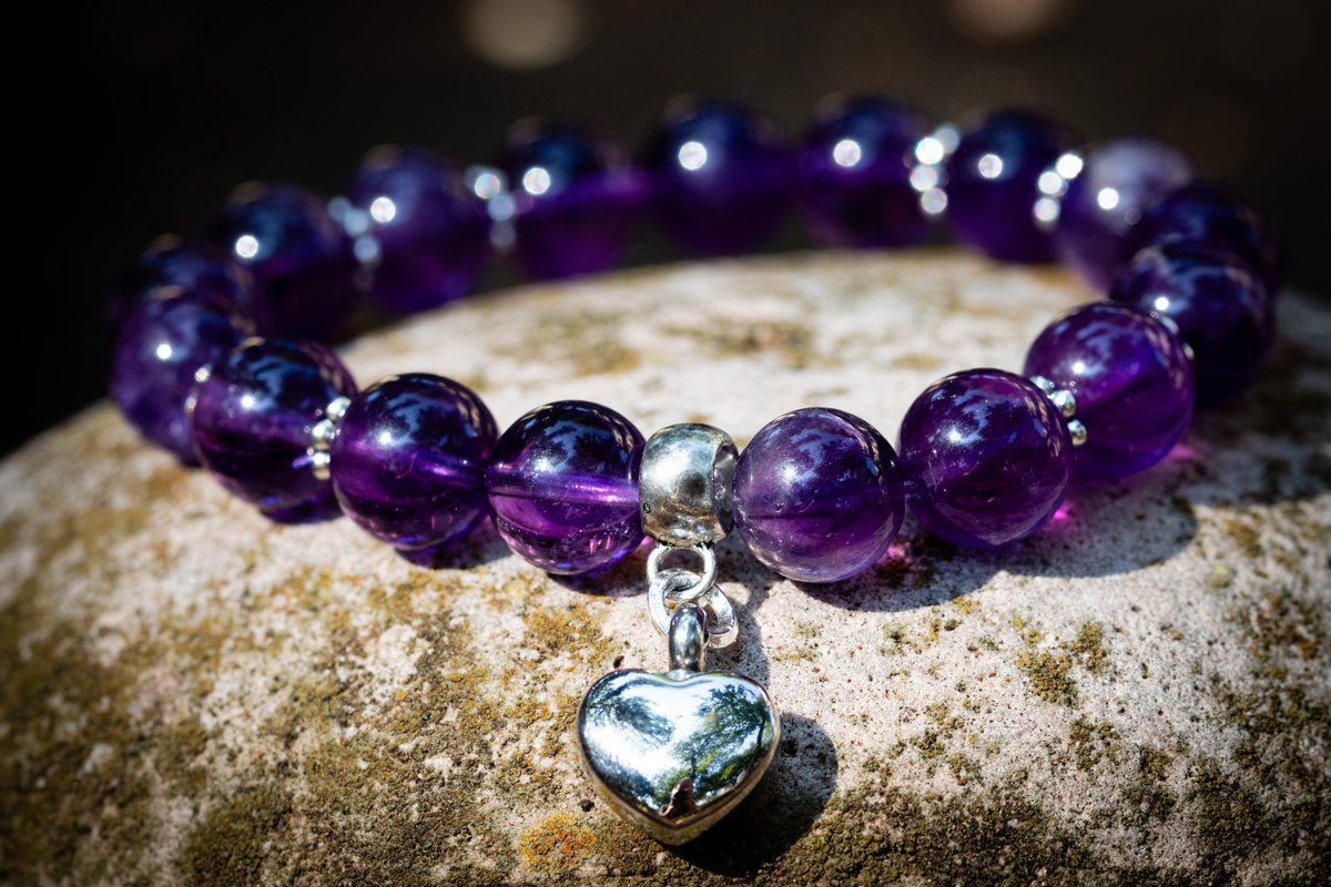 amethyst beaded bracelet with a silver heart urn charm on a stone surface
